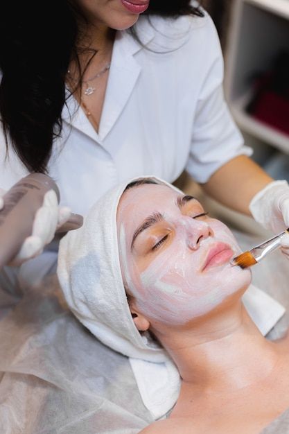 Free Photo | Beautician with a brush applies a white moisturizing mask to the face of a young girl client in a spa beauty salon